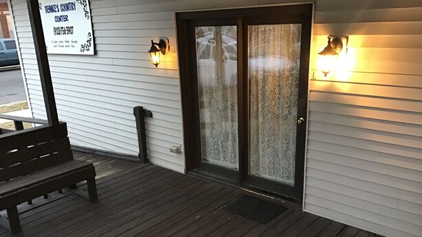 A wooden deck with a bench, a door with frosted glass, and two wall-mounted lights. - Behnke's Country Center, Reedsville WI. EAA, Green Bay Packers, Road America (Reedsville)
