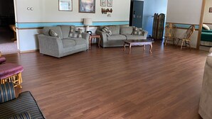 A spacious living room with two grey sofas, a wooden coffee table, and a wooden chair. There is a small table with a lamp, and a blue wall with framed pictures. - Behnke's Country Center, Reedsville WI. EAA, Green Bay Packers, Road America (Reedsville)