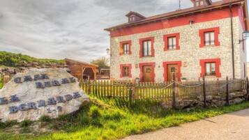 Experience the charm of Casa Rural Berardesa, a traditional stone building with a warm facade, surrounded by lush greenery and a wooden fence.