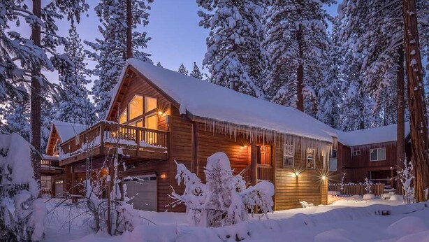 A log cabin with a wooden exterior, a balcony, and icicles hanging from the roof.