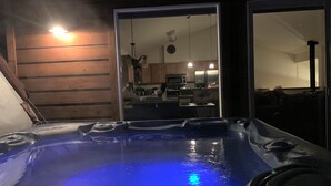 A hot tub with a wooden exterior wall and a kitchen visible through an open door.
