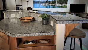 A modern kitchen with granite countertops, a wooden bowl, a potted plant, and a #laketahoelife sign on the wall.