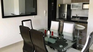 A modern kitchen with a refrigerator, microwave, and sink. There is a glass dining table with chairs and a large mirror on the wall. - Aparta Suite Ventus (Tunja)