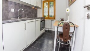 A compact kitchen with white cabinets, a grey countertop, and a window with curtains. - Bergfink Obergeschoss by Interhome (Grächen)