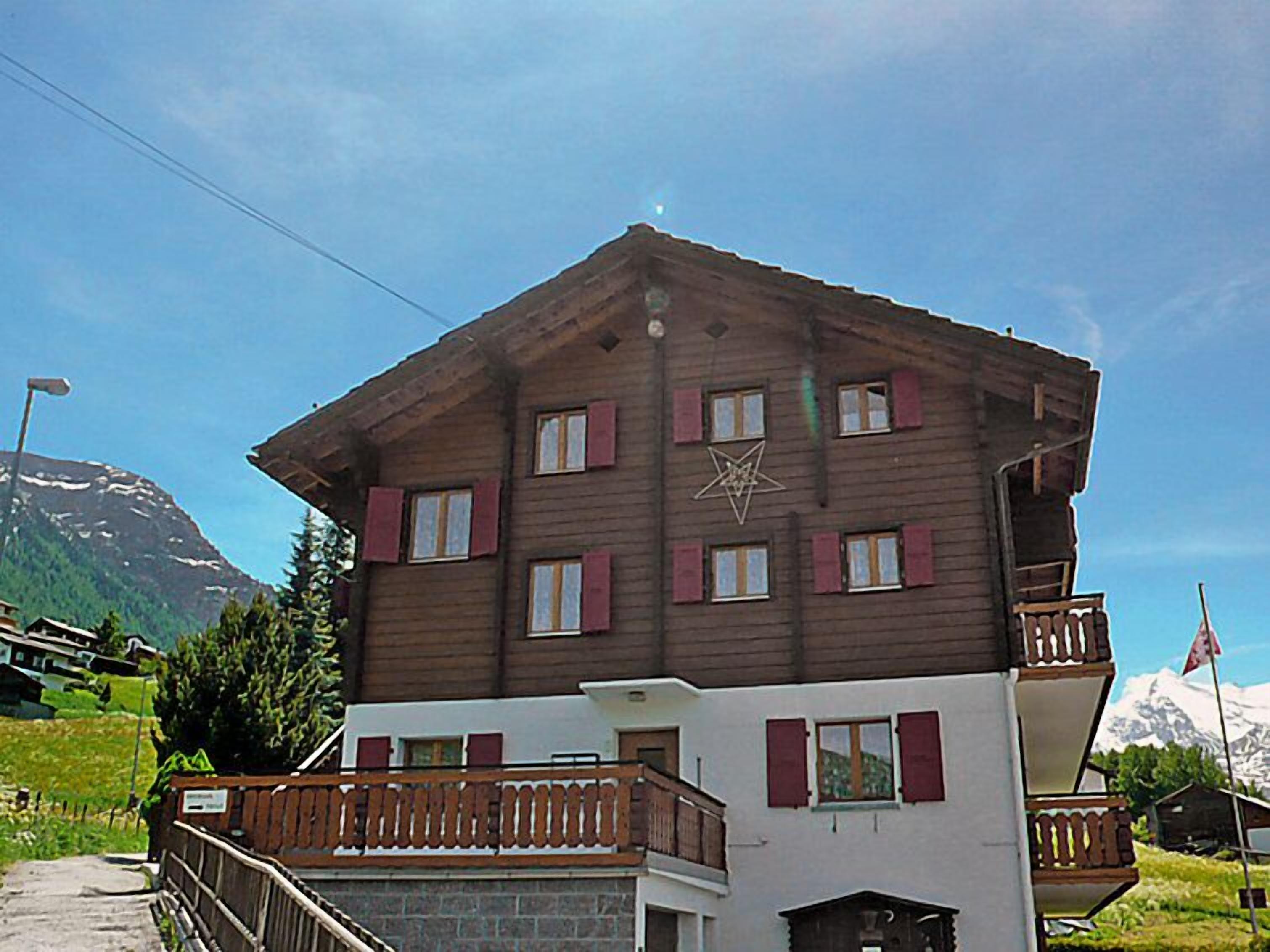 A two-story chalet with a wooden facade, red shutters, and a balcony.