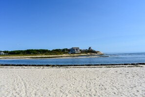 A beach with a house on a cliff overlooking the ocean.
