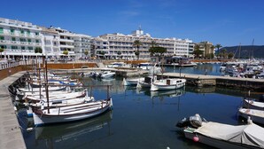 Un puerto deportivo con barcos amarrados, un hotel llamado HOTEL CALA BONA al fondo, y un cielo azul despejado.
