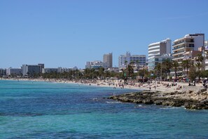 A beach with clear blue water, sandy shore, and buildings in the background. - Apartment CarpeDiem Cala Bona Mallorca Cala Millor (Son Servera)