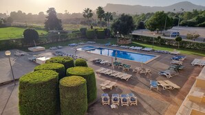 Zona de piscina con tumbonas y una piscina, rodeada de setos bien cuidados y vistas a colinas distantes.