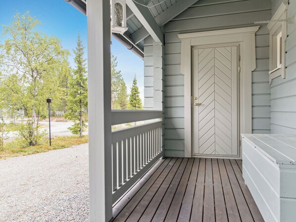 A porch with a wooden deck, a white door with a chevron pattern, and a clear sky.