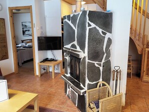 A living room with a stone fireplace, a television, and a wooden staircase.