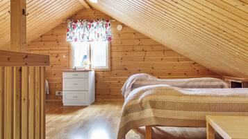 A cozy attic bedroom with wooden walls and sloped ceilings, featuring two beds, a dresser, and a window with floral curtains.