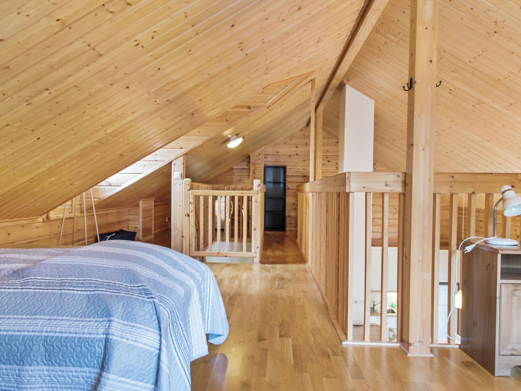 Un interior de madera con techo inclinado, una cama con manta a rayas, un escritorio con lámpara y una pequeña kitchenette.