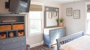 Une chambre à coucher avec un lit, une commode, un téléviseur et une fenêtre avec des stores.