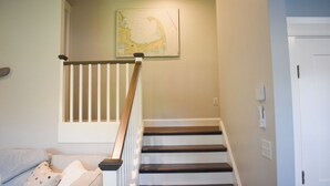 Un escalier avec des rampes blanches et des marches sombres, un mur de couleur claire et une porte sur la droite.