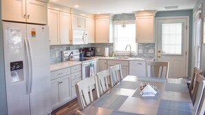 Une cuisine moderne avec des meubles blancs, un grand îlot central et un coin repas comprenant une table et des chaises.