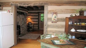 A rustic kitchen with a stone wall, wooden beams, a wooden table with a plant, and a refrigerator. - Tavern River Cabin, Historical,  Riverfront, Log, Hottub, Large Stone Fireplace (Luray)