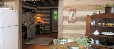 A rustic kitchen with a stone wall, wooden beams, a wooden table with a plant, and a refrigerator.