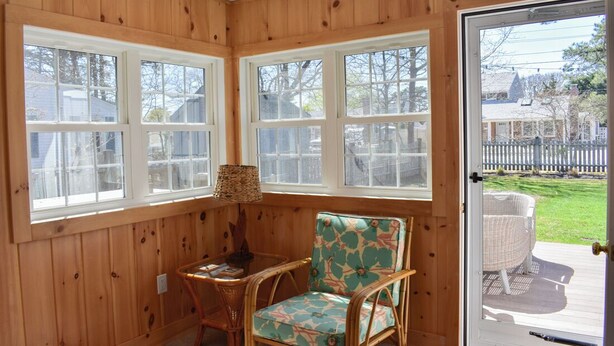 Une pièce d’angle aux murs en bois, avec un fauteuil en osier, une table et une porte donnant sur l’extérieur.