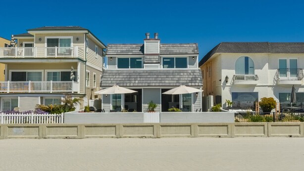 A beachfront property with a two-story building, a covered patio with umbrellas, and a white fence. - Oceanfront South Mission Beach Vacation Rental on the Sand 2737 (San Diego)