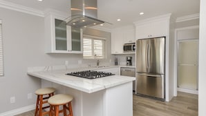 A modern kitchen with a central island, stainless steel appliances, and wooden stools. - Oceanfront South Mission Beach Vacation Rental on the Sand 2737 (San Diego)
