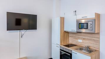 Eine kleine Küche mit integriertem Mikrowellenherd, Backofen und Spüle, einer Holzarbeitsplatte und einem flachbildfernseher an der Wand.