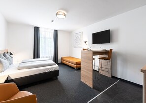 A modern hotel room with a bed, a desk, a TV, and a window with curtains. - Apartimo Landshut (Landshut)