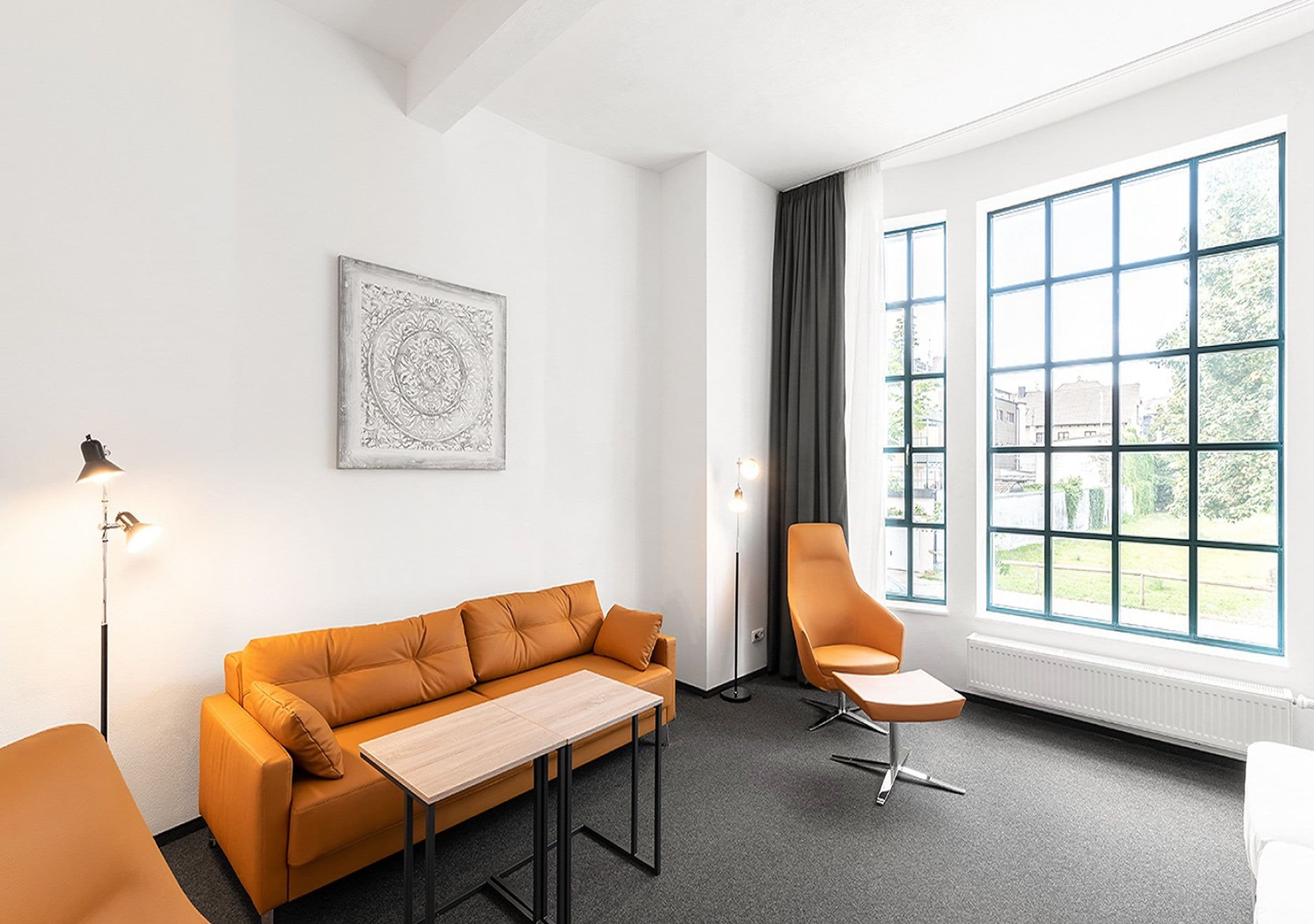 A modern room with a sofa, a table, a chair, and large windows offering a view of the outdoors.