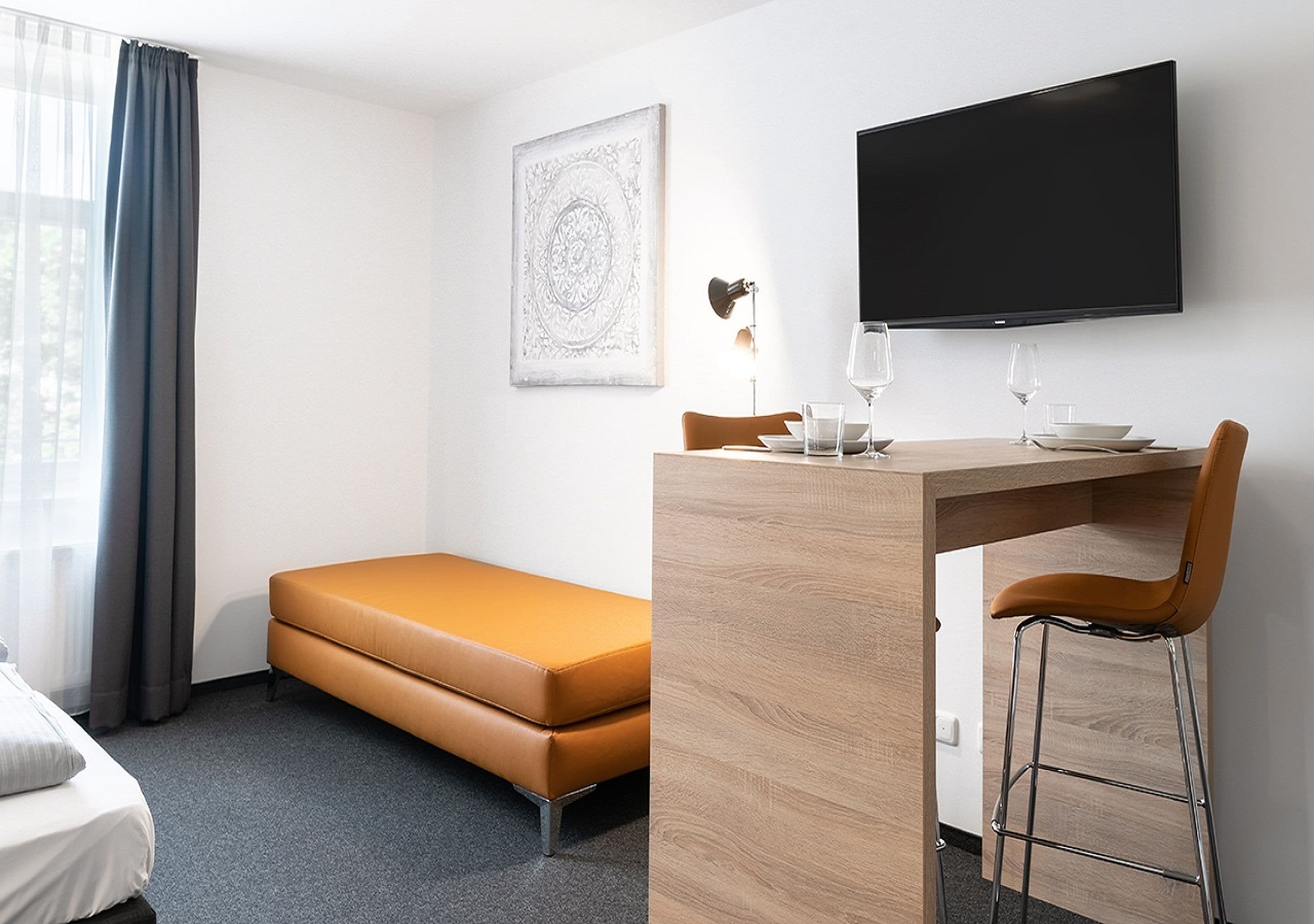 A hotel room with a bed, a sofa, a desk with a chair, a flat-screen TV, and a framed picture on the wall.