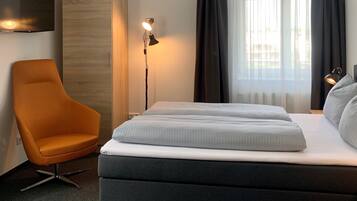 A modern hotel room with a large bed, a chair, a TV, and a window with curtains.