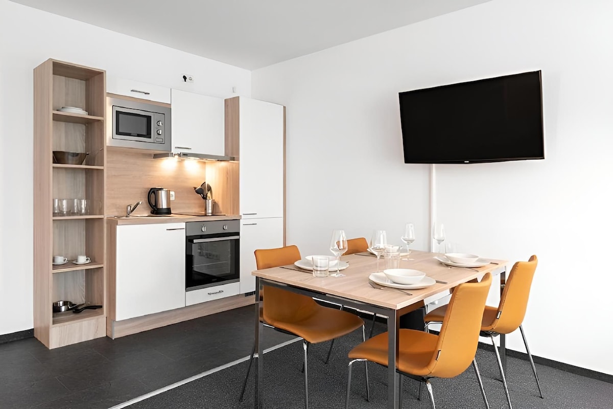 Eine moderne Küche mit Mikrowelle, Backofen und Kaffeemaschine, einem Esstisch mit Stühlen und einem an der Wand befestigten Flachbildfernseher.