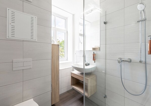 A modern bathroom with a glass shower enclosure, a white sink, and a window providing natural light. - Apartimo Landshut (Landshut)