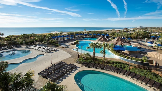 Een resort met meerdere zwembaden, ligbedden en palmbomen.