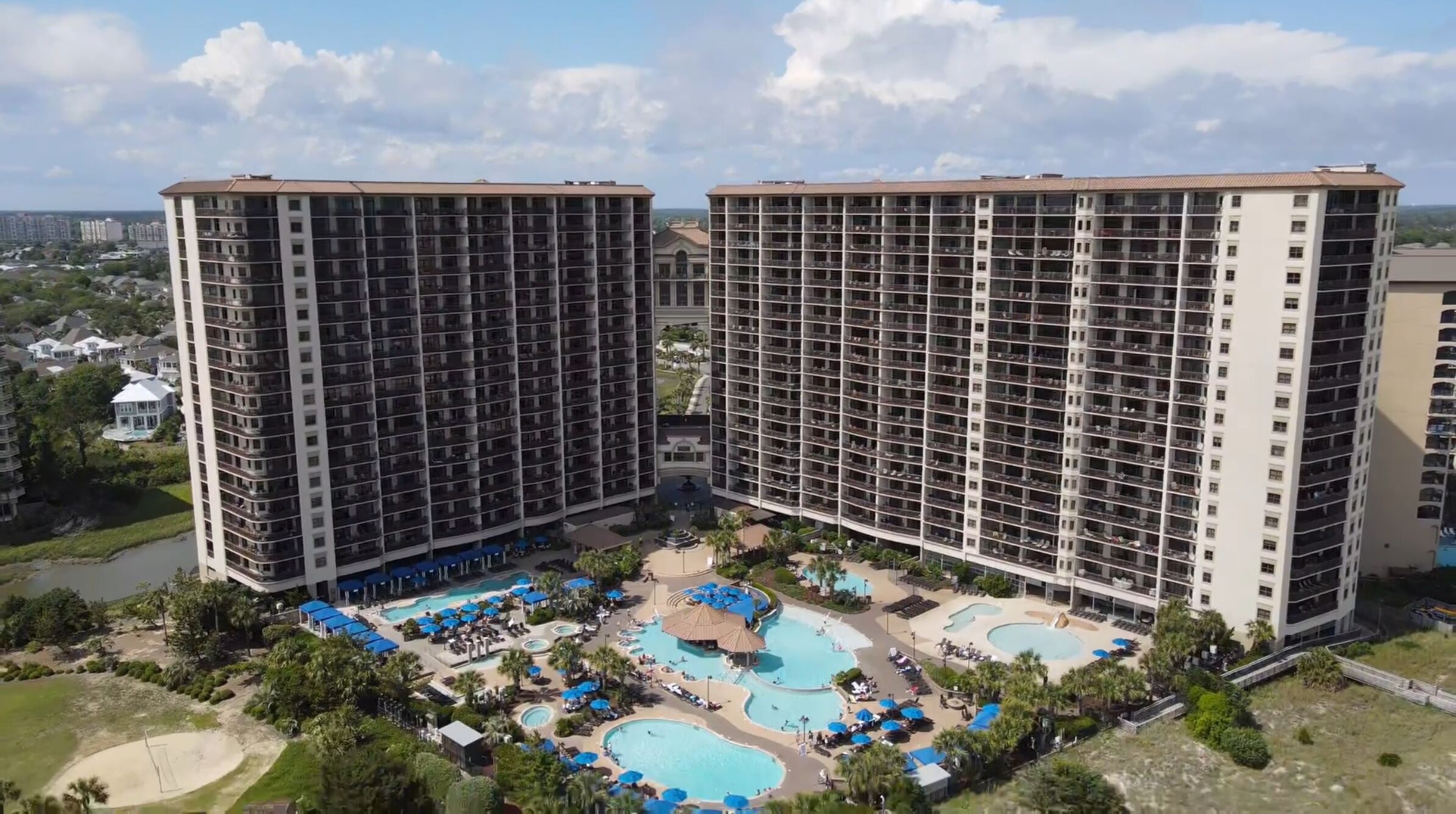 Un hôtel de grande hauteur, doté de nombreux étages, d’une cour intérieure avec des piscines et entouré de verdure.