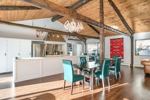 Un vaste espace dédié à la salle à manger, avec un plafond en bois, un îlot central et des chaises de couleur turquoise.