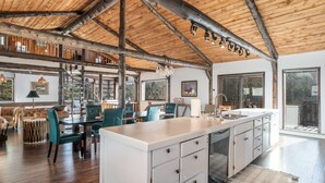A spacious kitchen with a large island, wooden beams on the ceiling, and a view of the outdoors through large windows. - Luxury Mountain Retreat Near Estes Park Stunning Views, Perfect Family Getaway (Allenspark)