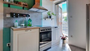 A modern kitchen with white cabinets, a stove, oven, and a sink. There are two potted plants on the counter.