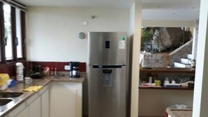 A compact kitchen with a stainless steel refrigerator, a sink, and a countertop with various items. - ANGRA DOS REIS. CONDITION PORTOGALO RJ CASA DO GUGU  (ANGRA DOS REIS)