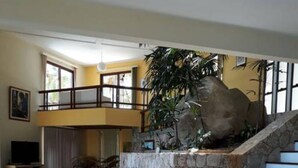 A spacious living area with a stone staircase, a dining table, and a large plant. - ANGRA DOS REIS. CONDITION PORTOGALO RJ CASA DO GUGU  (ANGRA DOS REIS)