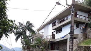 A two-story building with balconies, a stone retaining wall, and a road with a yellow line. - ANGRA DOS REIS. CONDITION PORTOGALO RJ CASA DO GUGU  (ANGRA DOS REIS)