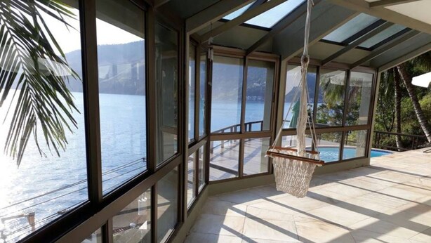 A sunlit room with large windows overlooking a body of water and mountains. - ANGRA DOS REIS. CONDITION PORTOGALO RJ CASA DO GUGU  (ANGRA DOS REIS)