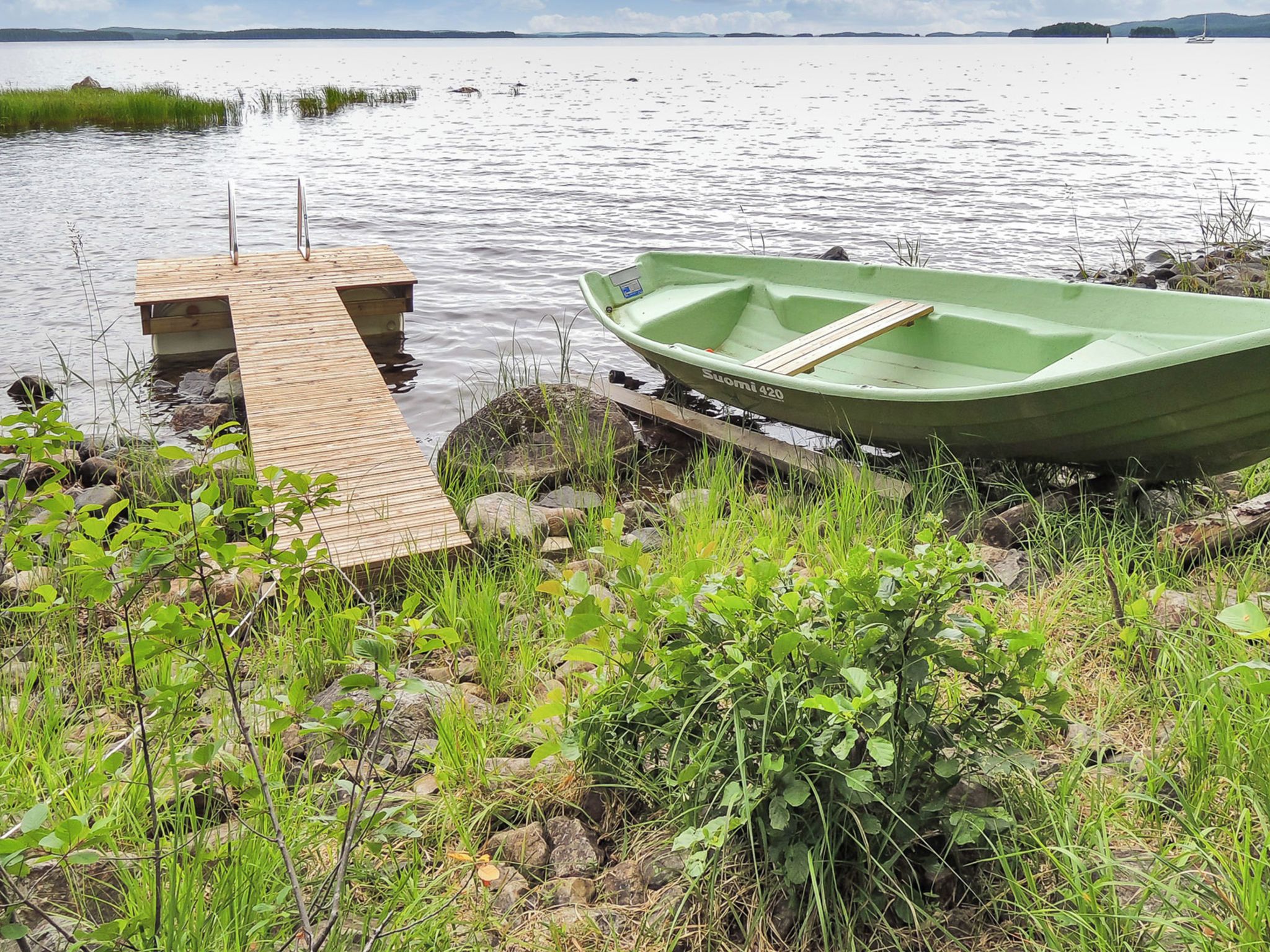 A green boat on a wooden dock by a calm lake with a clear sky.