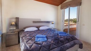 Une chambre à coucher avec un lit, des tables de chevet et une vue sur l’extérieur, accessible par une porte-fenêtre coulissante.