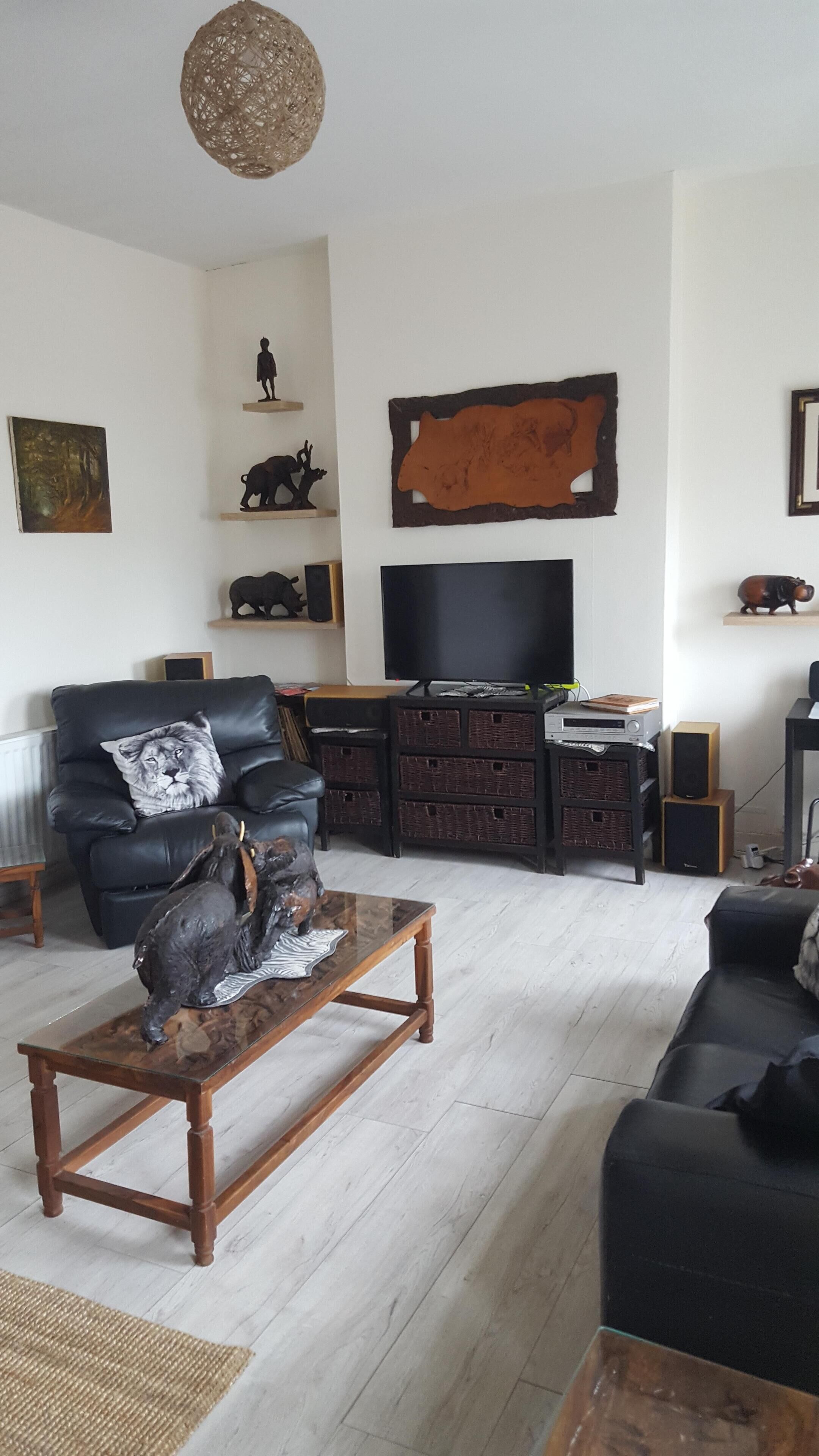 Un soggiorno con un divano in pelle, un tavolino in legno, una televisione e diversi oggetti decorativi sugli scaffali.