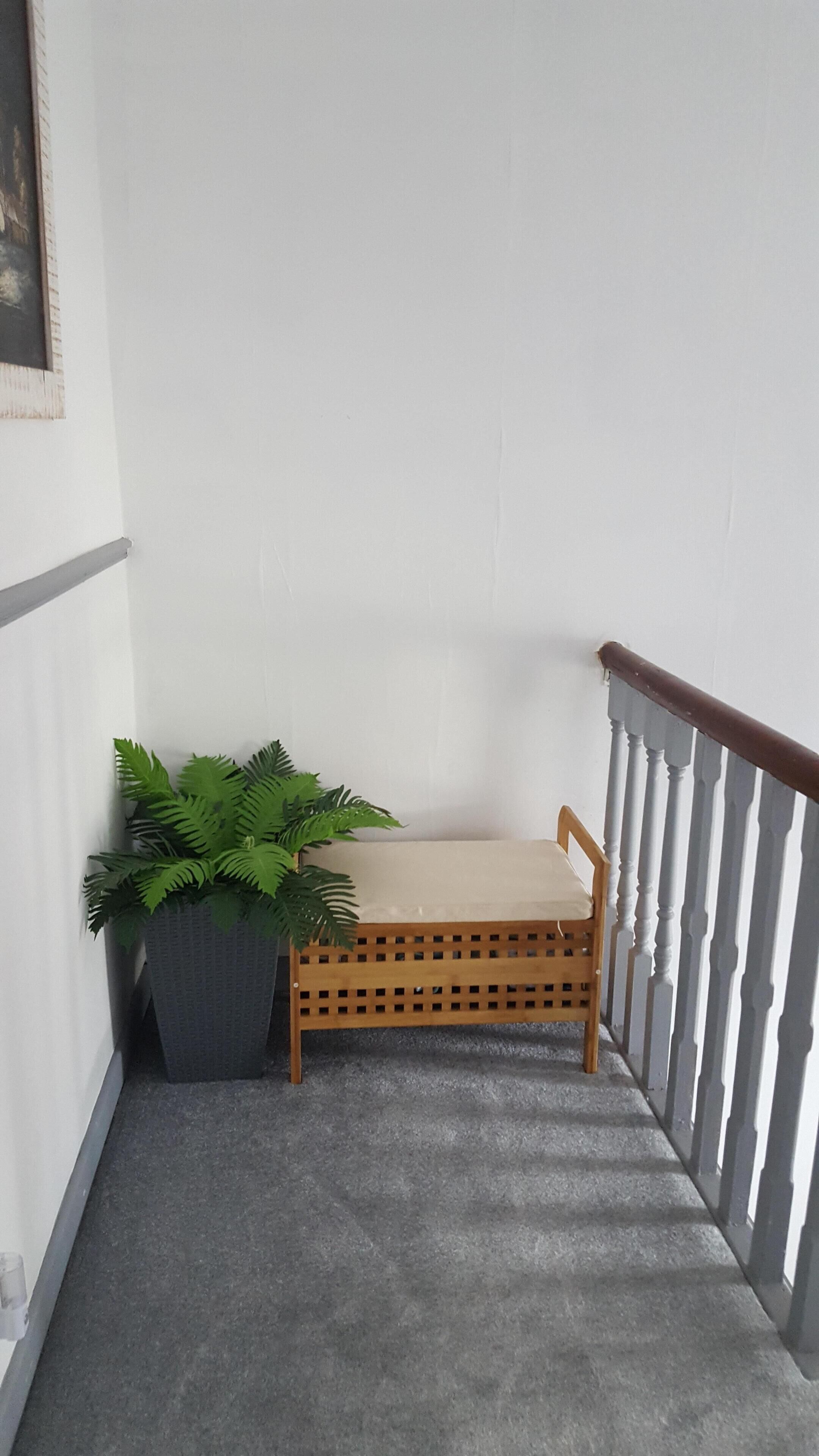 En hjørne bænk med en potteplante, et træværk gelænder og en hvid væg.