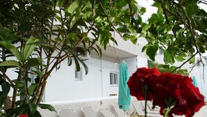 A terrace with lounge chairs and a white building in the background. - Spacious apartment just 2 min walk from the beach! (Plakias)