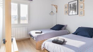 Un dormitorio con dos camas, una ventana, un radiador y una lámpara fijada a la pared.