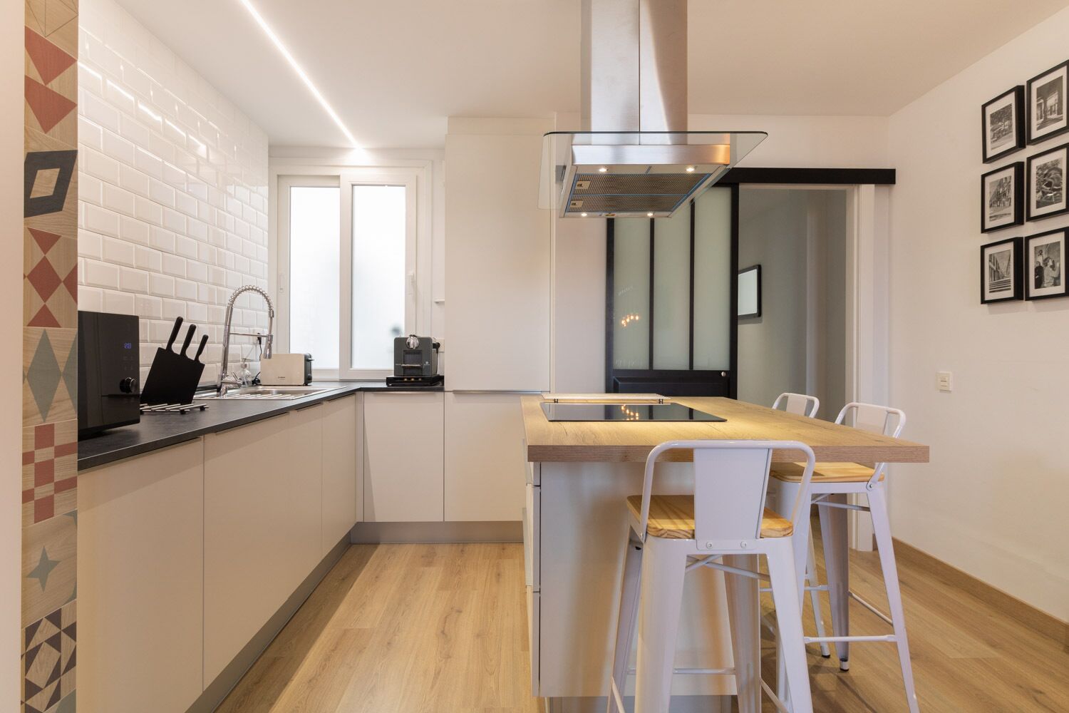 Een moderne keuken met een centraal eiland, witte barkrukken en een eettafel.