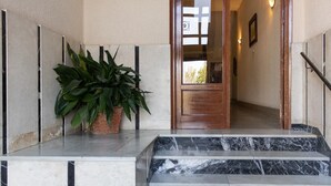 Una escalera de mármol que conduce a una puerta de madera con un cartel con el número 9, una planta en maceta y una pared con una lámpara.