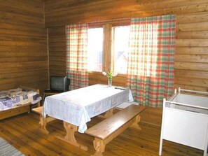 Una cabaña con interior de madera, una cama, una mesa con mantel, un banco, un televisor y cortinas de cuadros.